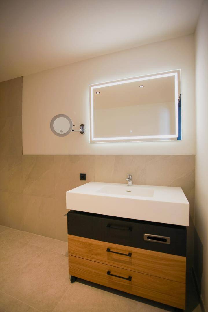 Modernes Badezimmer mit stilvollem Waschtisch, beleuchtetem Spiegel und Wandfliesen.