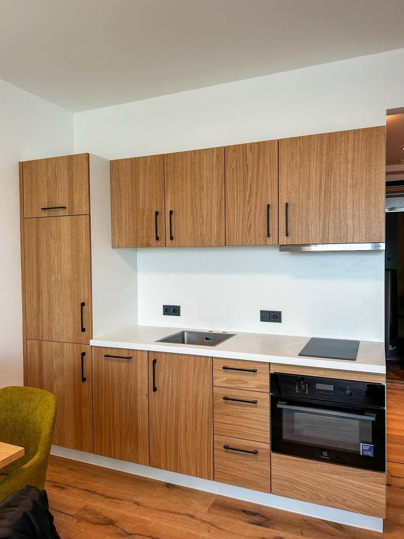 Moderne Einbauküche mit Holzfronten, Induktionskochfeld und integriertem Backofen.