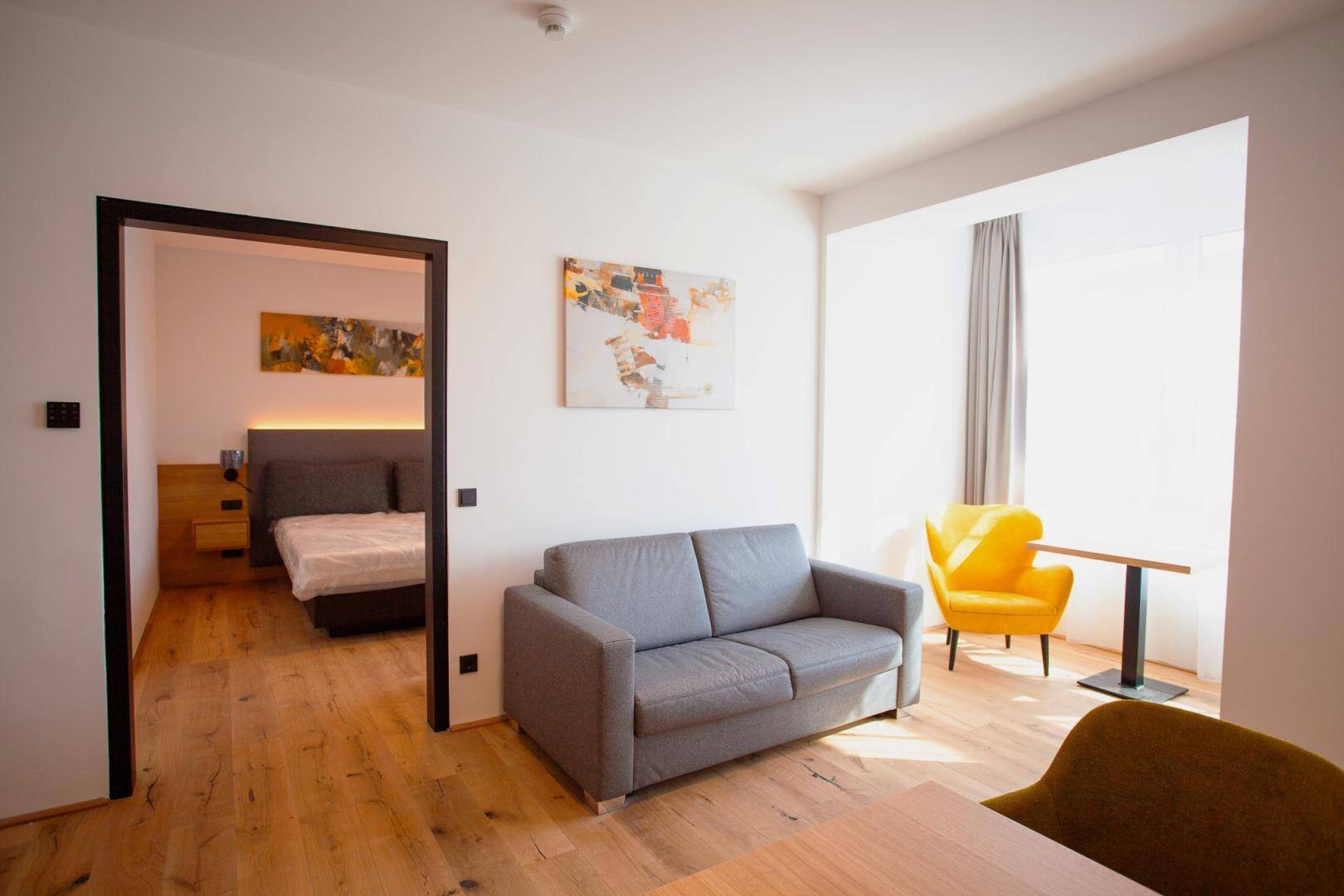 Gemütliches Wohnzimmer mit Sofa, Sessel und Zugang zu einem angrenzenden Schlafzimmer.