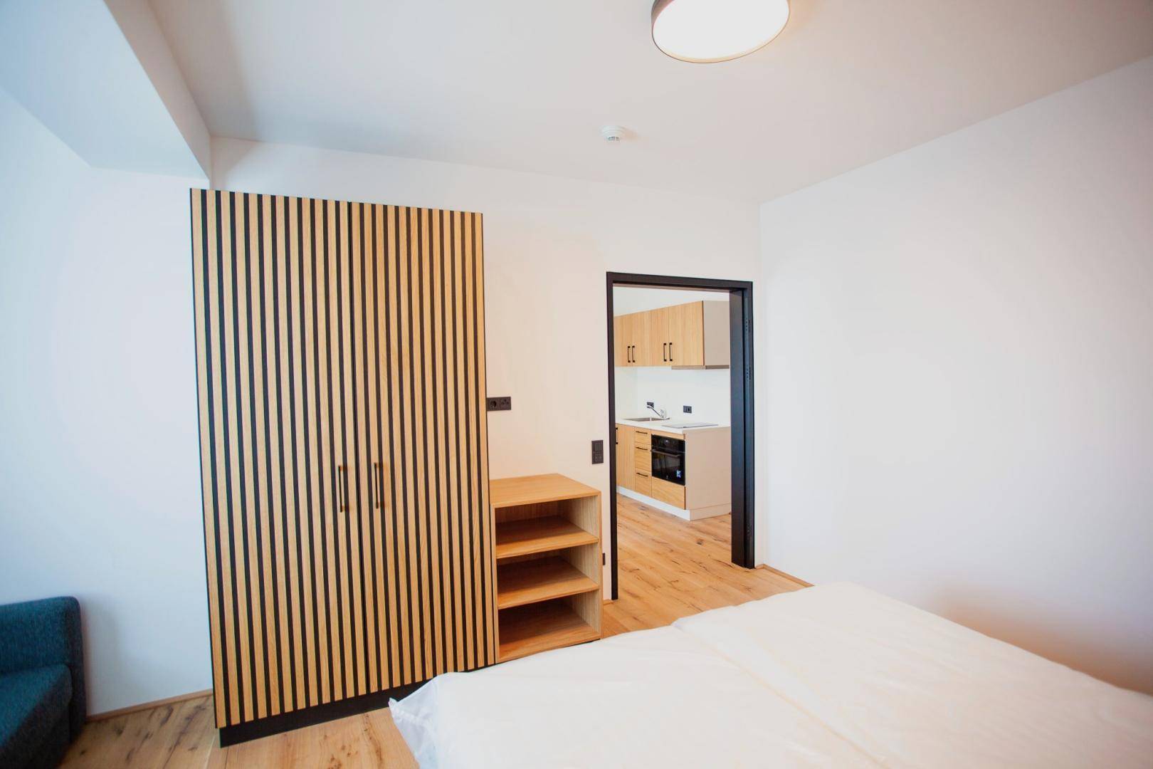 Schlafzimmer mit modernem Kleiderschrank und Blick in die angrenzende Küchenzeile.