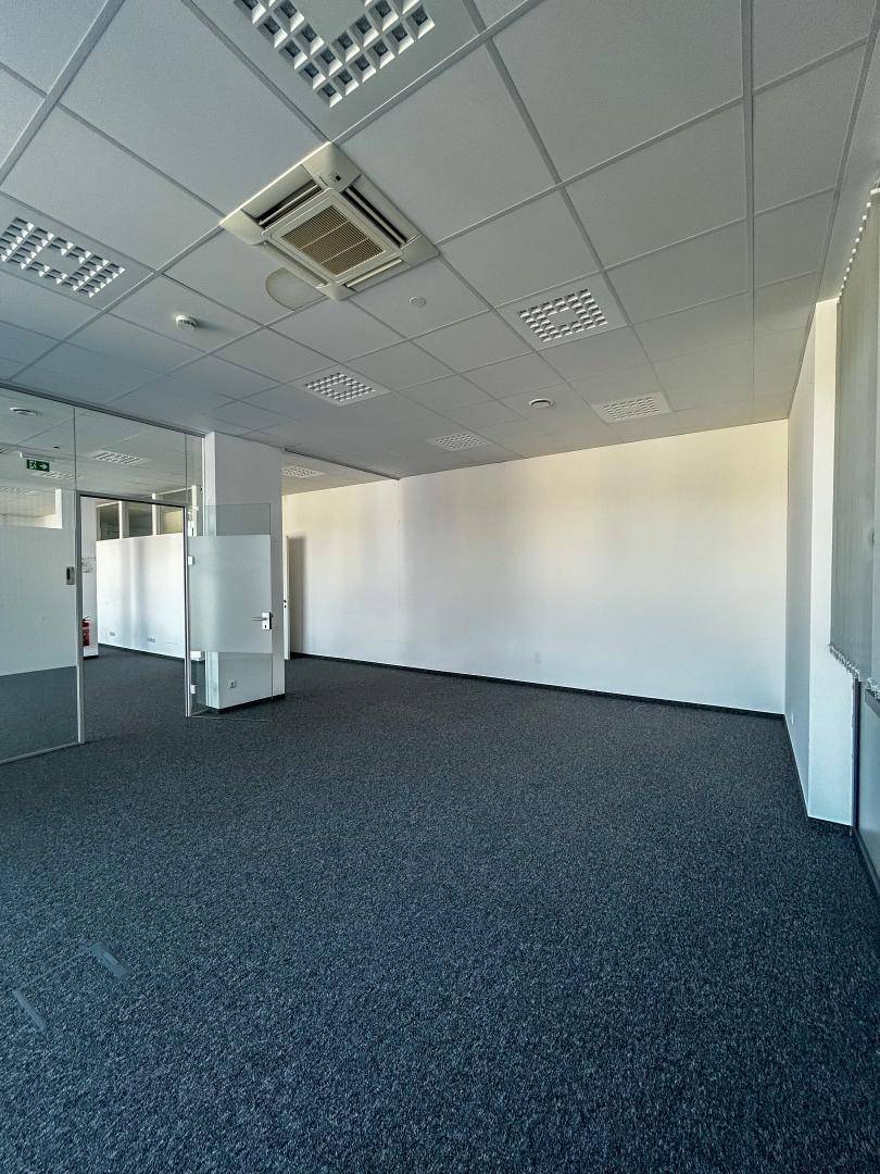 Heller Büroraum mit Teppichboden, Glaswänden und Klimaanlage an der Decke, bietet flexible Arbeitsbereiche.