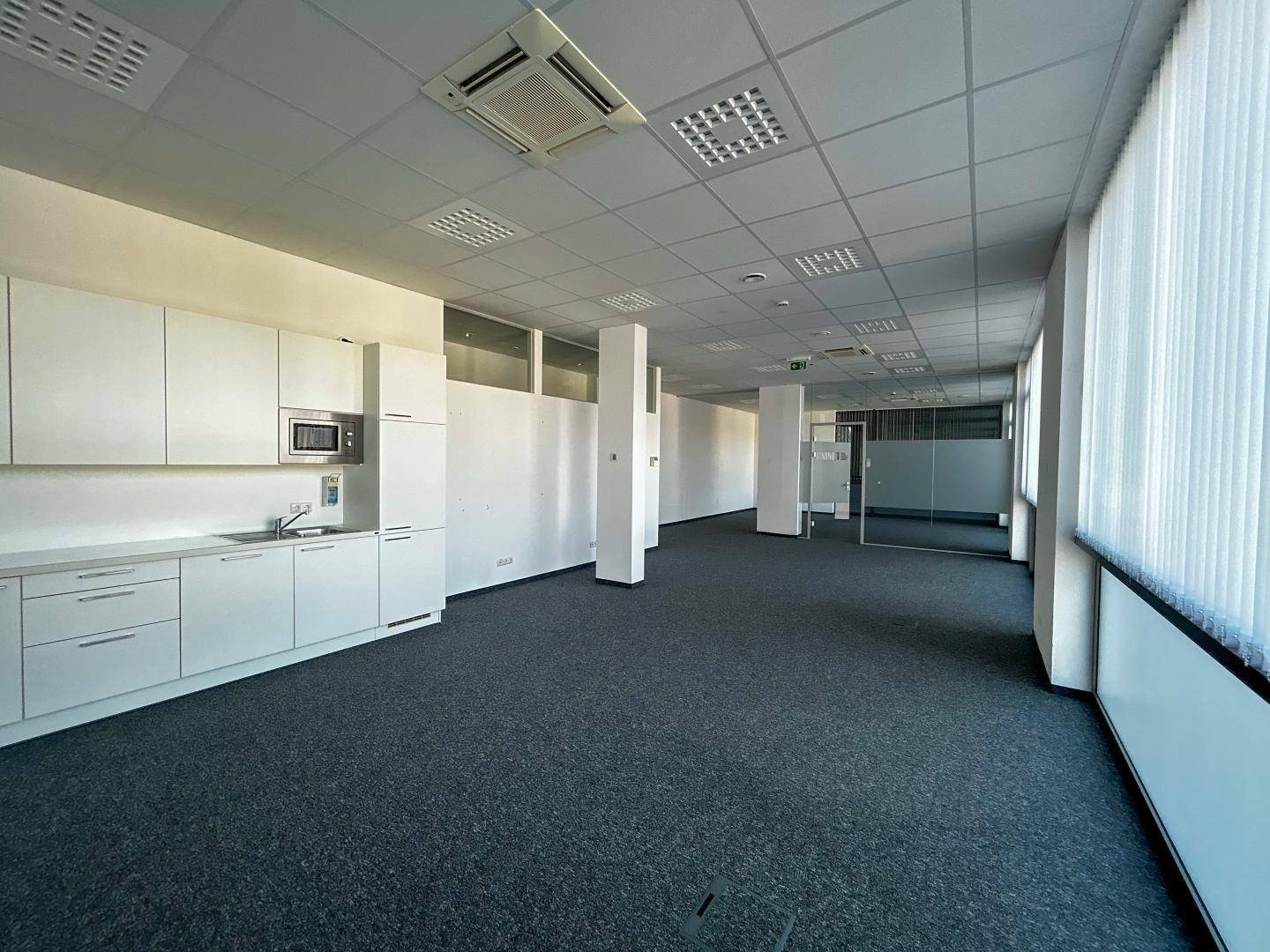 Großes Büro mit integrierter Küchenzeile, Teppichboden und großen Fenstern, ideal für Pausenbereiche.