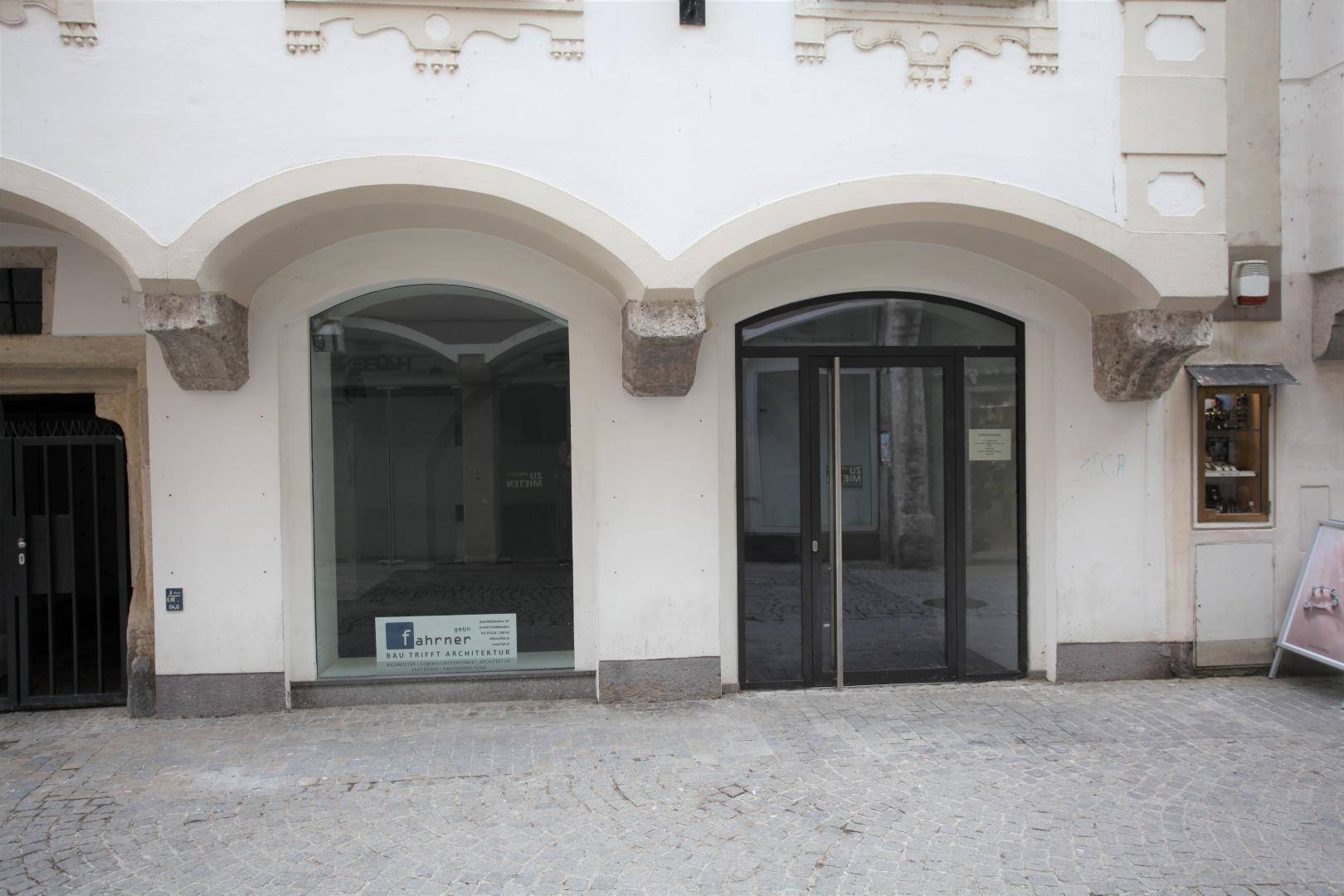 Fassade eines Gebäudes mit zwei großen Bogenfenstern und einem Eingang zu Geschäftsräumen.