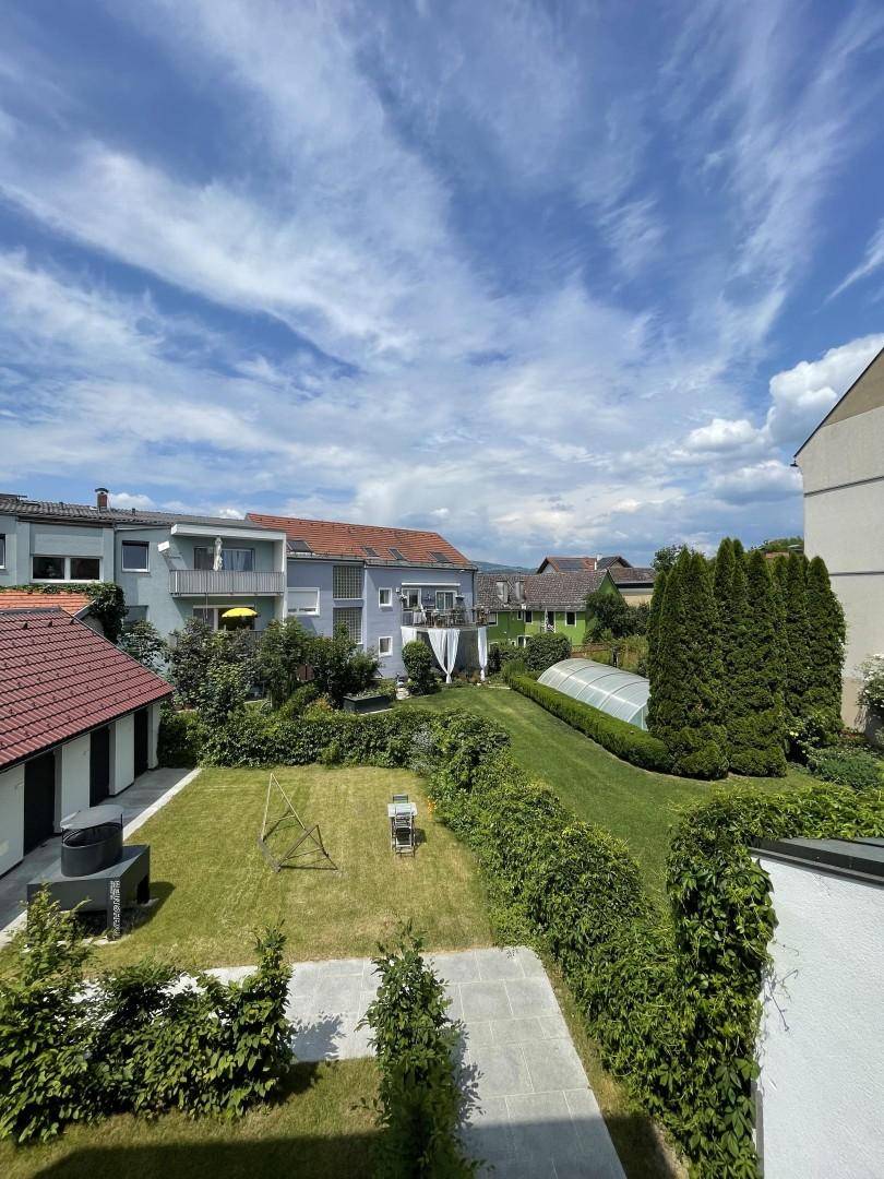Weitläufiger Gartenbereich mit Rasenflächen, Hecken und Blick auf die umliegenden Häuser.