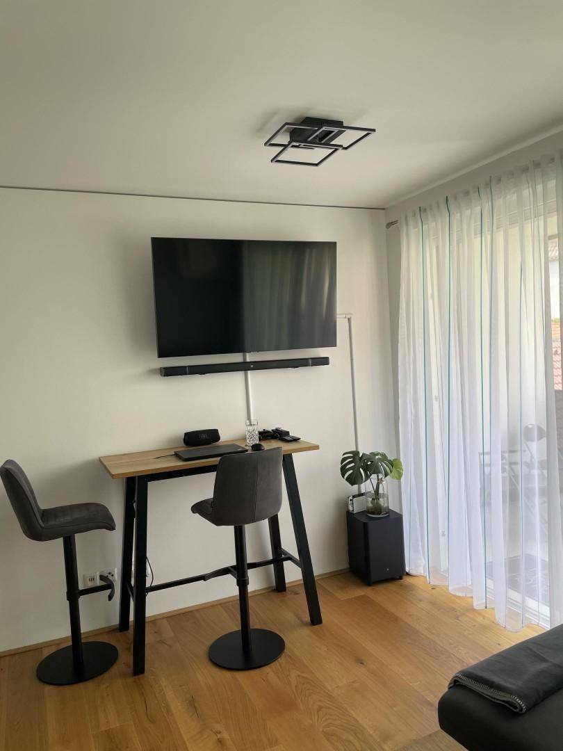 Moderner Wohnbereich mit wandmontiertem Fernseher und einem hohen Tisch mit Barhockern.