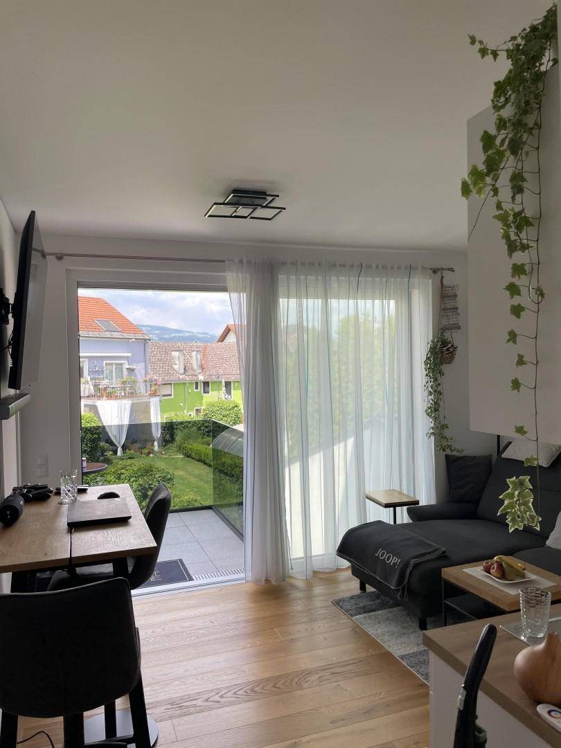 Helles Wohnzimmer mit großen Glasfronten und Zugang zu einer Terrasse mit Gartenblick.