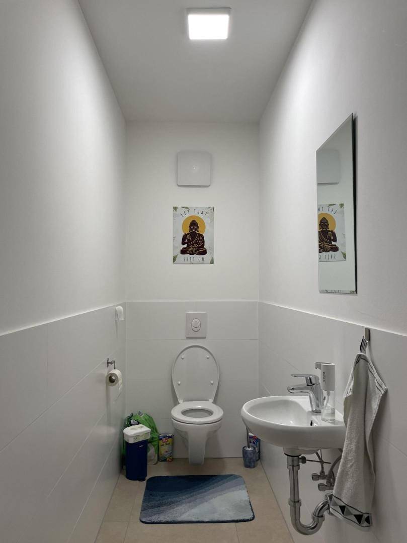 Separates WC mit wandhängender Toilette und kleinem Handwaschbecken.