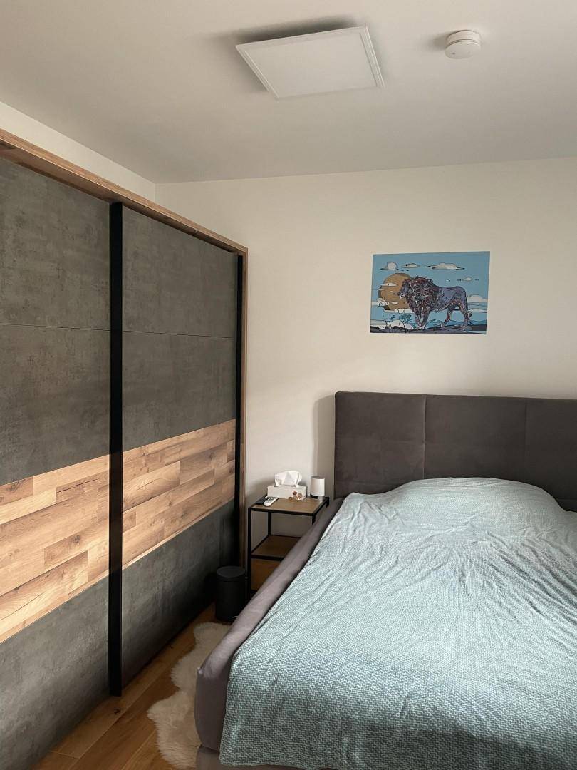 Schlafzimmer mit modernem Bett und großem Einbauschrank aus Holz und Betonoptik.