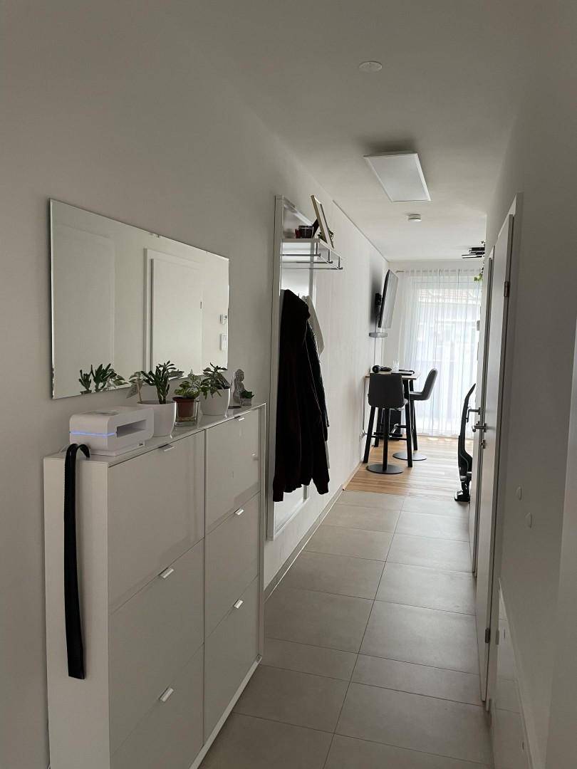 Heller Flur mit Schuhschrank, Spiegel und Garderobe, der zum Wohnbereich führt.