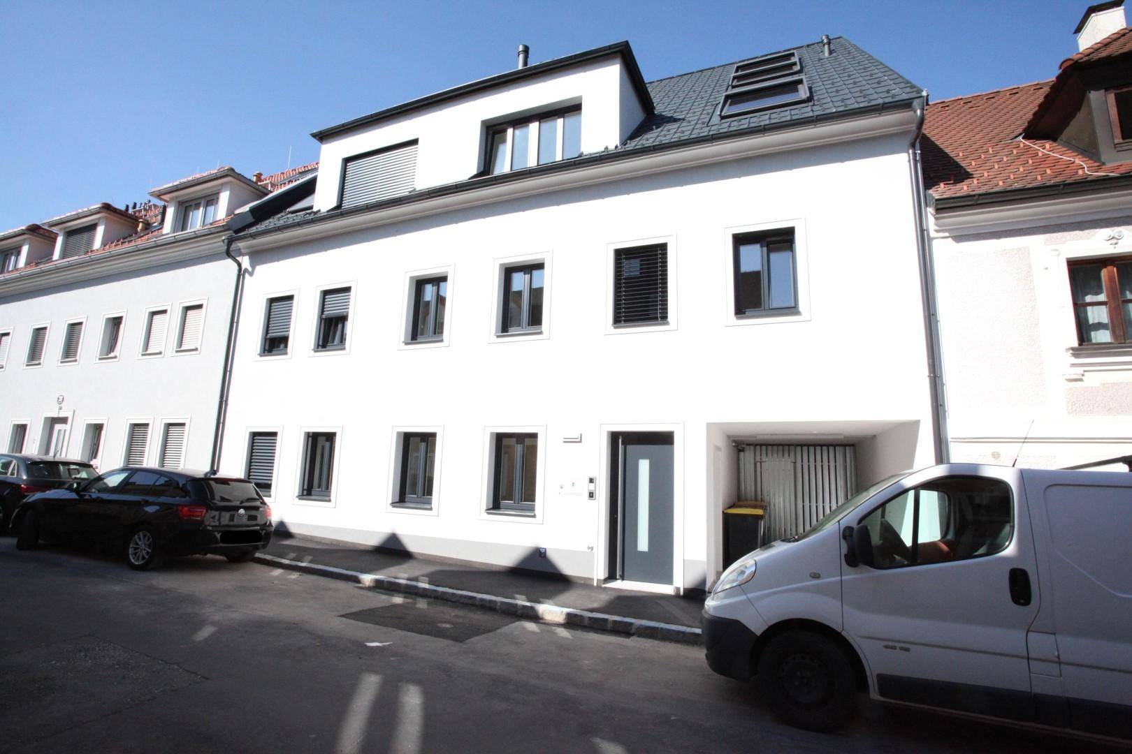 Modernes weißes Gebäude mit Satteldach, Dachfenstern und integrierter Garage an einer Straße.