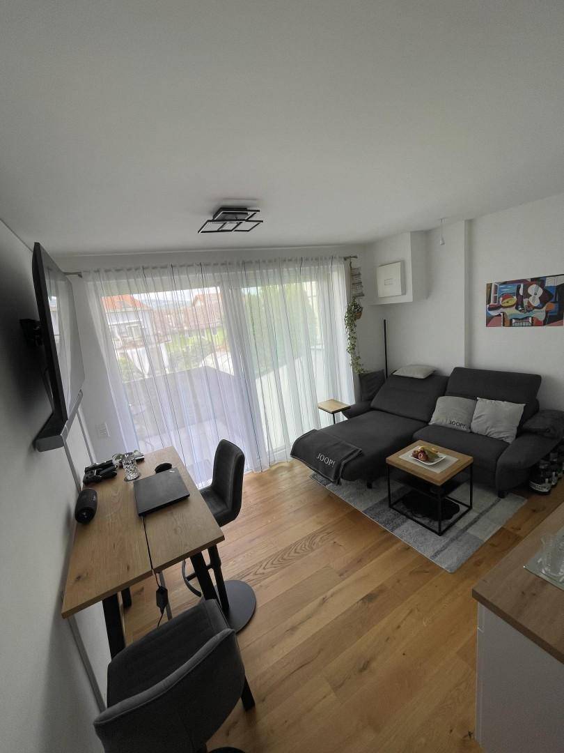 Geräumiges Wohnzimmer mit Sofa, Fernseher und viel Tageslicht durch große Fenster.