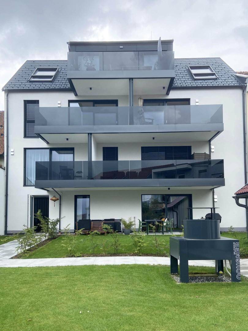 Moderne Gebäudefassade mit mehreren Balkonen und einem gepflegten Gartenbereich.