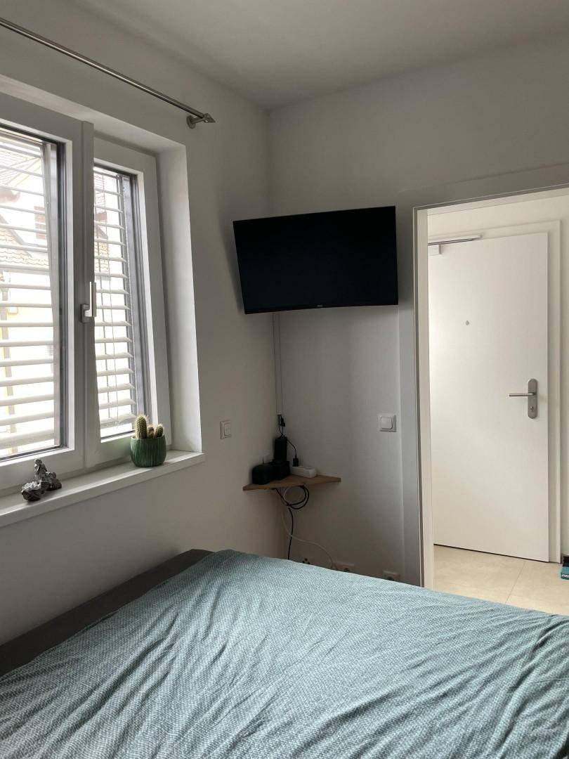 Schlafzimmer mit Fenster, Jalousien und einem wandmontierten Fernseher.