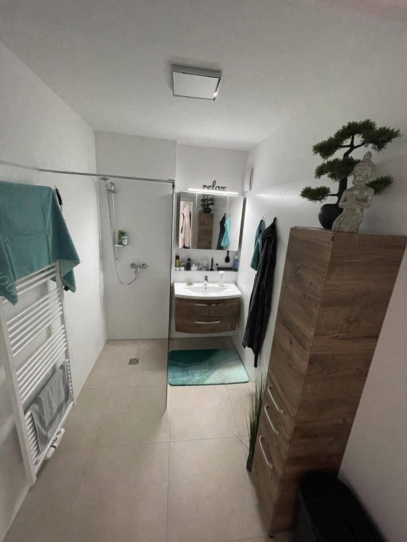 Helles Badezimmer mit moderner Einrichtung, begehbarer Dusche und Holzschrank.