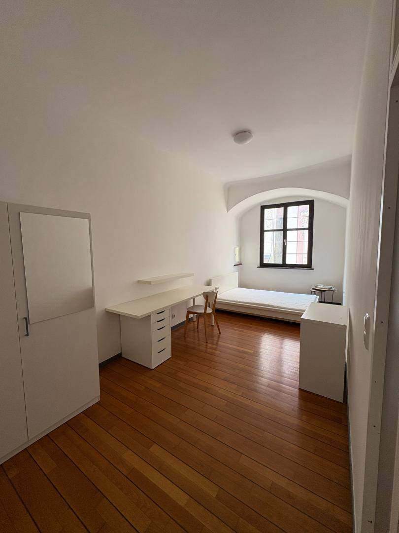 Helles Schlafzimmer mit Holzboden, Schreibtisch und Fenster mit tiefer Laibung.