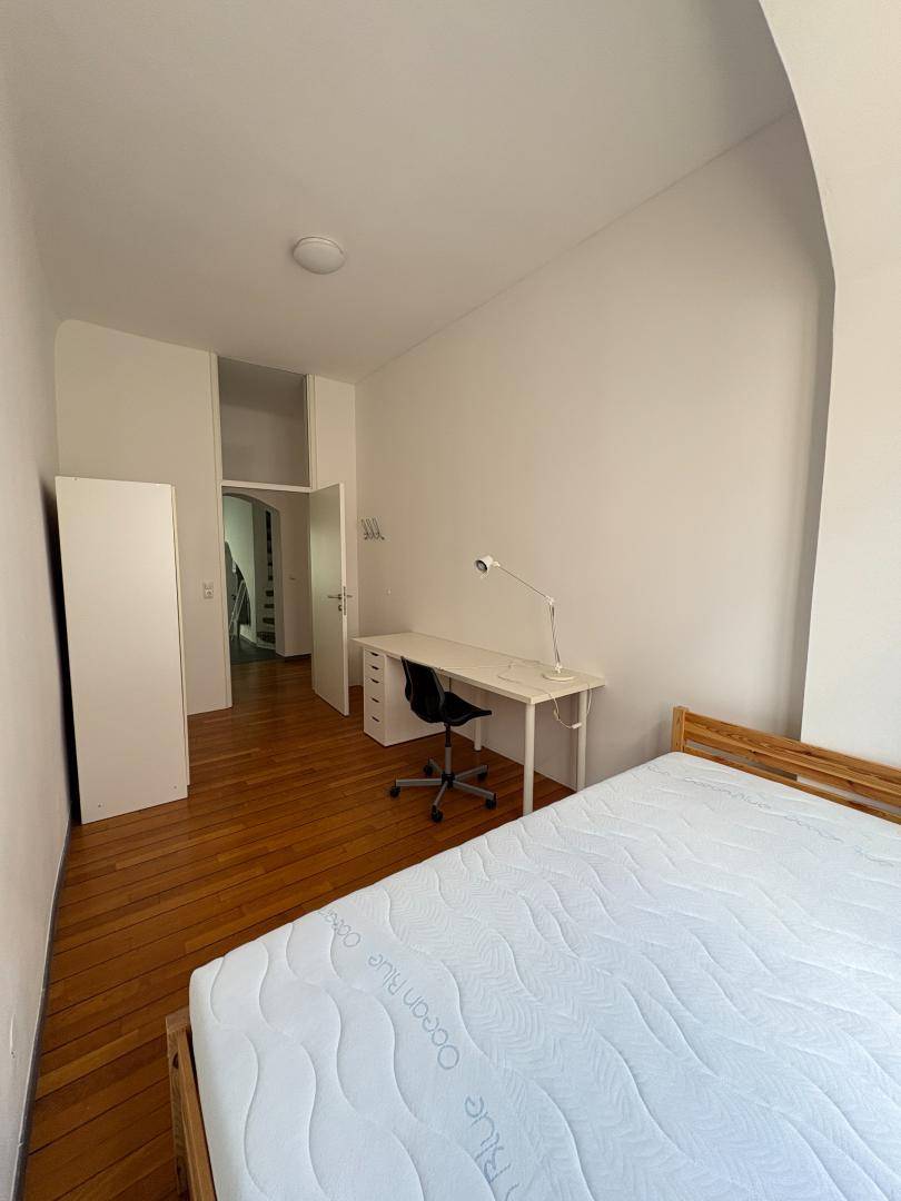 Schlafzimmer mit Holzboden, Schreibtisch und Blick in den Flur.