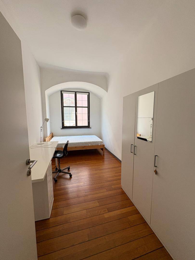 Gemütliches Schlafzimmer mit Holzboden, Fenster und integriertem Kleiderschrank mit Spiegel.