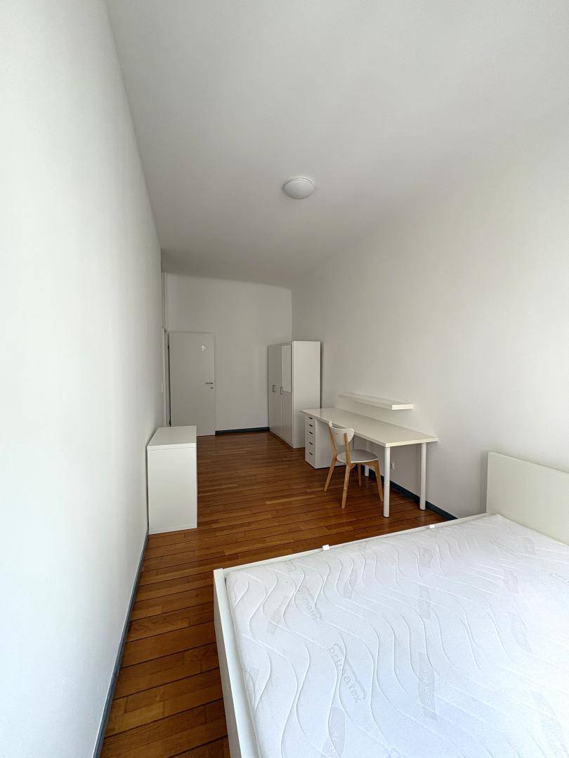 Einfaches Schlafzimmer mit Holzboden, weißem Bett und Schreibtisch.