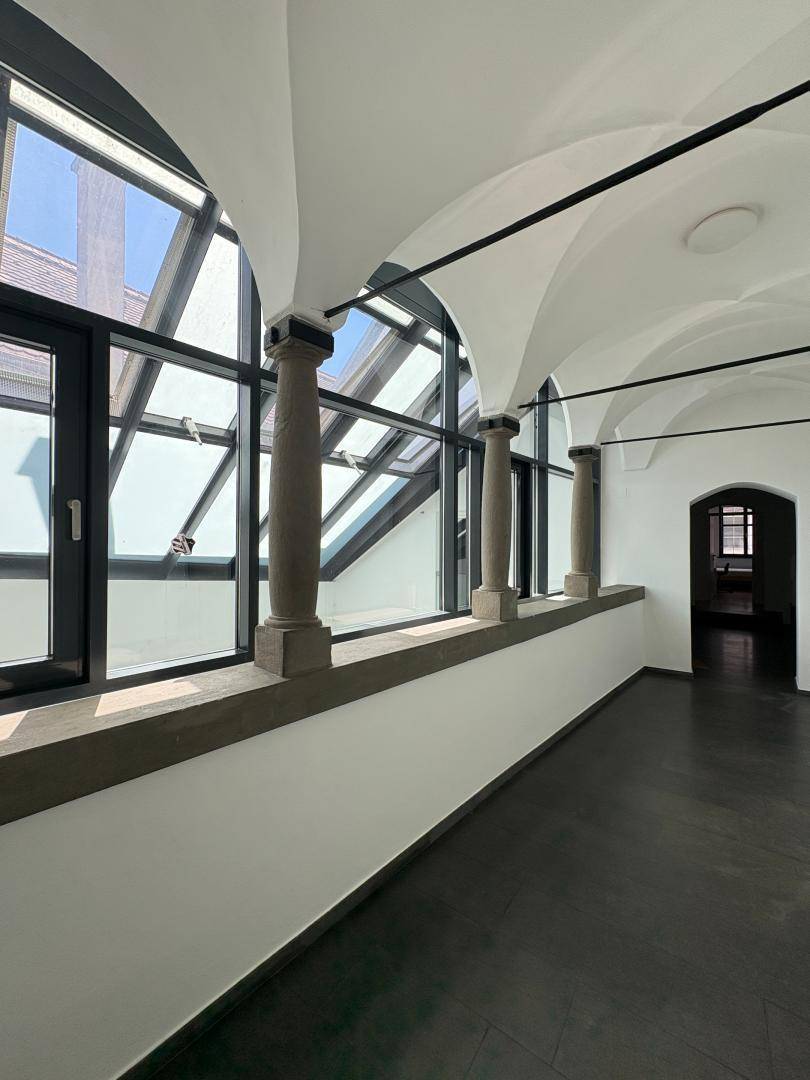 Heller Flur mit großen Fenstern, Säulen und gewölbter Decke.