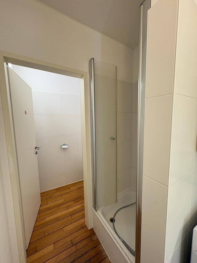 Badezimmer mit Duschkabine und Holzboden, offen zum Flur.