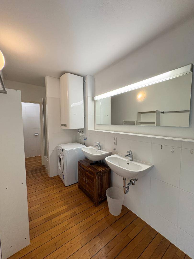 Geräumiges Badezimmer mit zwei Waschbecken, Waschmaschine und Holzboden.