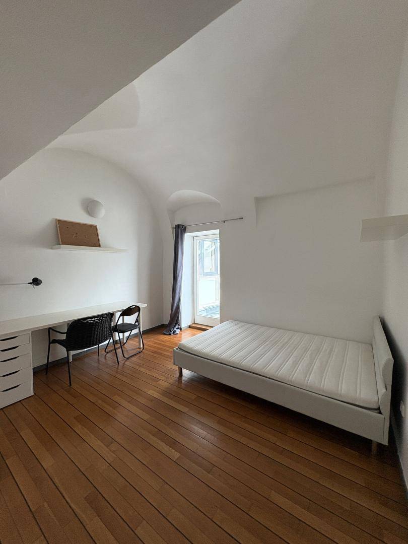 Schlafzimmer mit Holzboden, gewölbter Decke und Zugang zu einem kleinen Balkon oder Fenster.