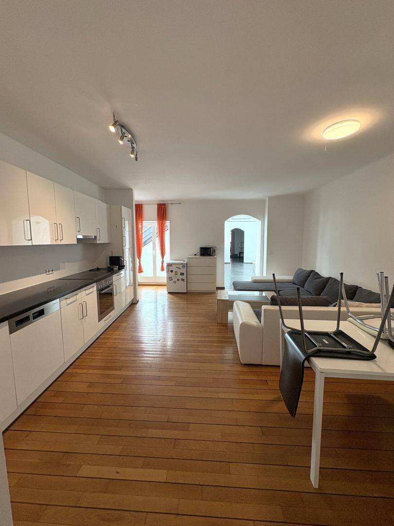 Offener Wohn- und Essbereich mit integrierter Küche, Holzboden und Sofa.