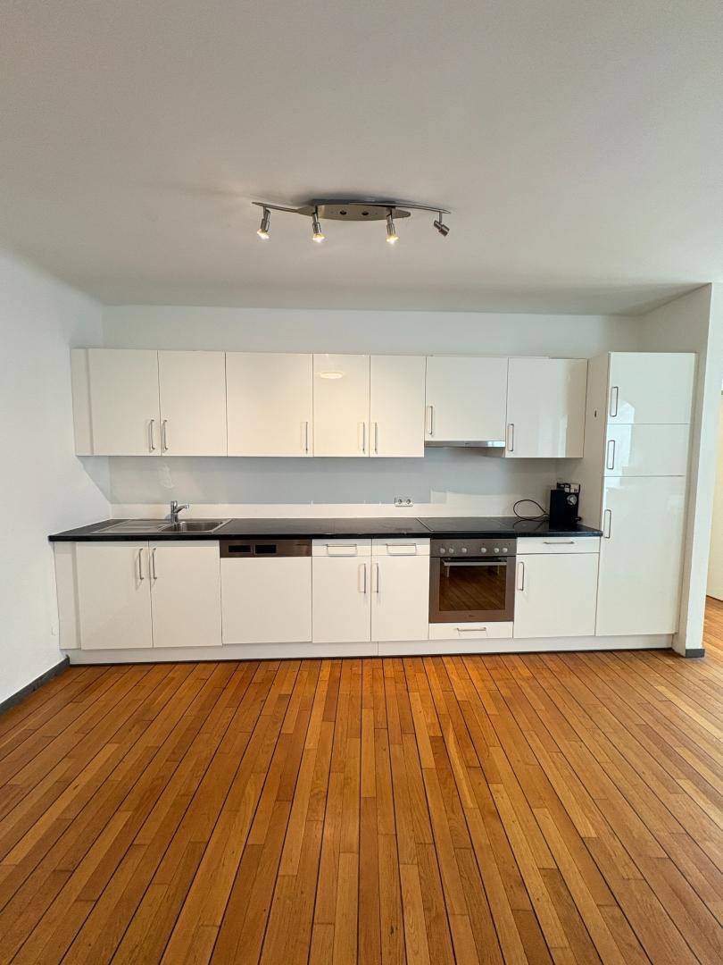 Moderne Einbauküche mit weißen Hochglanzfronten und dunkler Arbeitsplatte.
