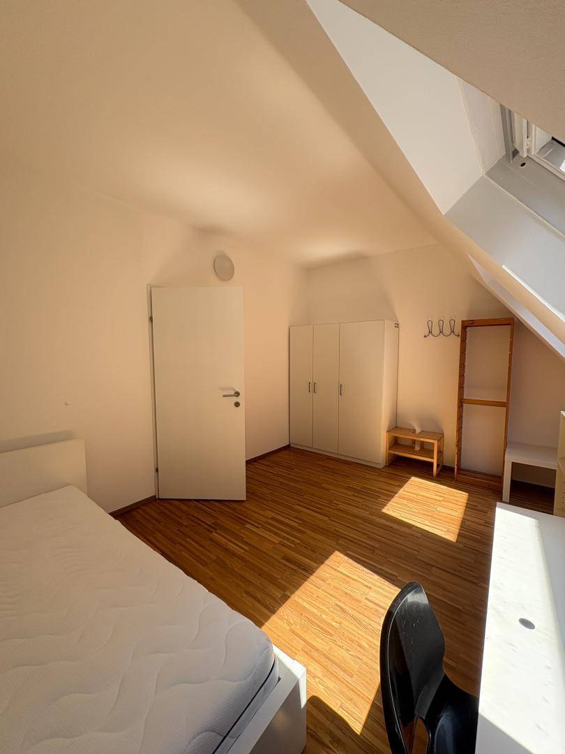 Helles Schlafzimmer mit Dachschräge, Parkettboden und weißem Kleiderschrank.