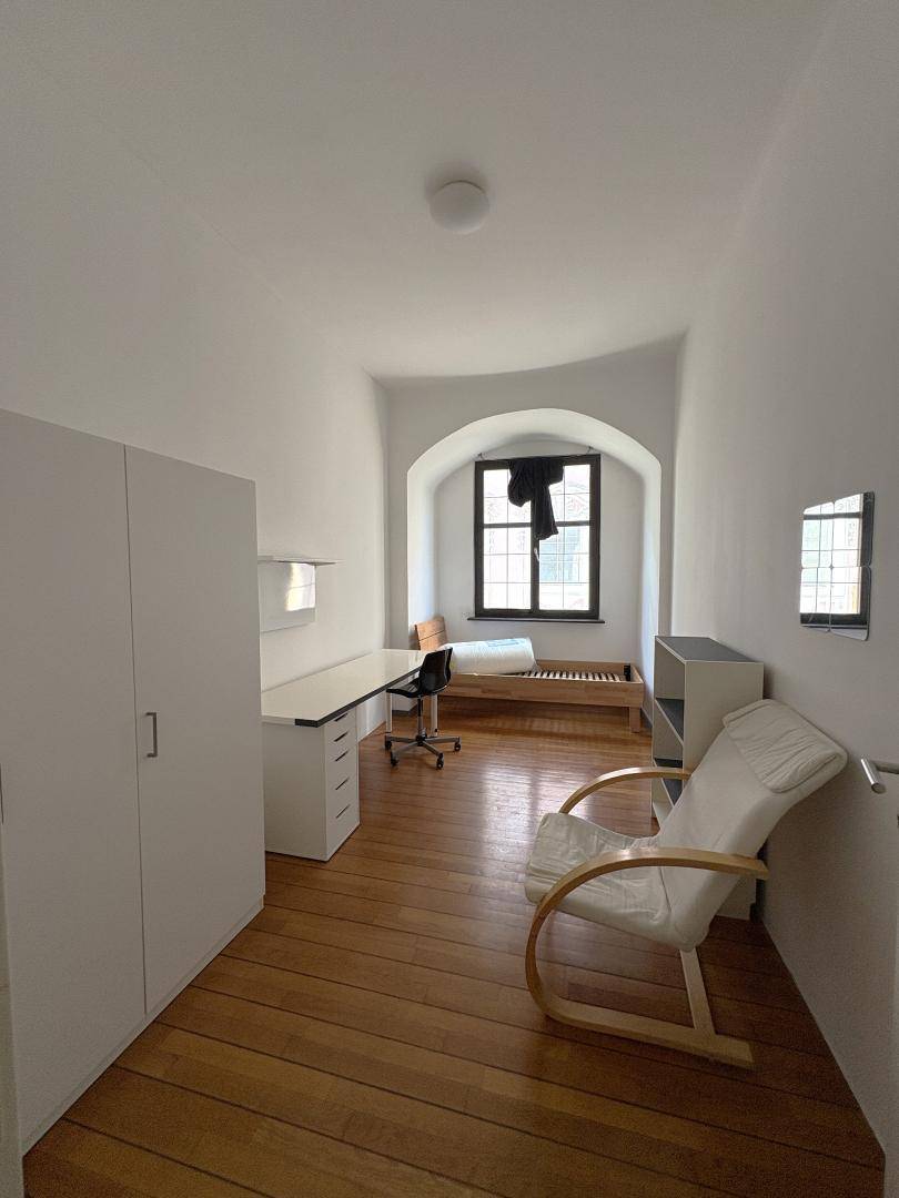 Geräumiges Schlafzimmer mit Parkettboden, Schreibtisch und Fenster.