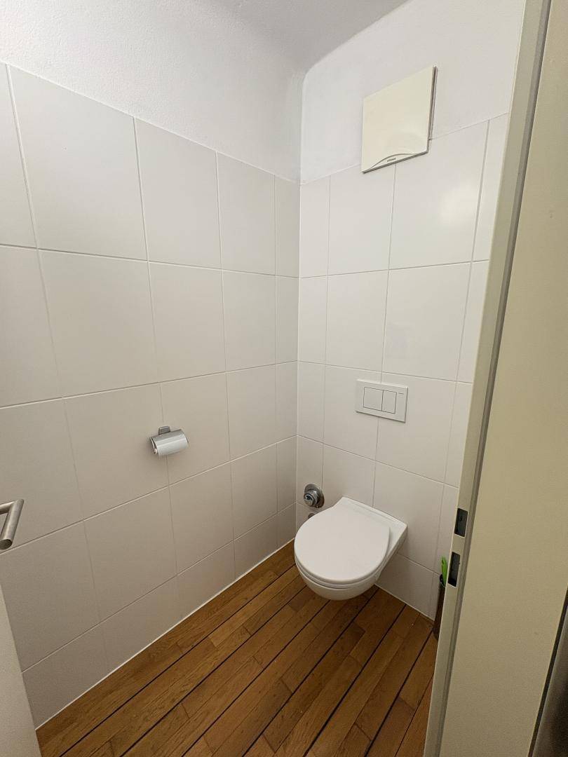 Separate Toilette mit Wand-WC und Fliesen an den Wänden.