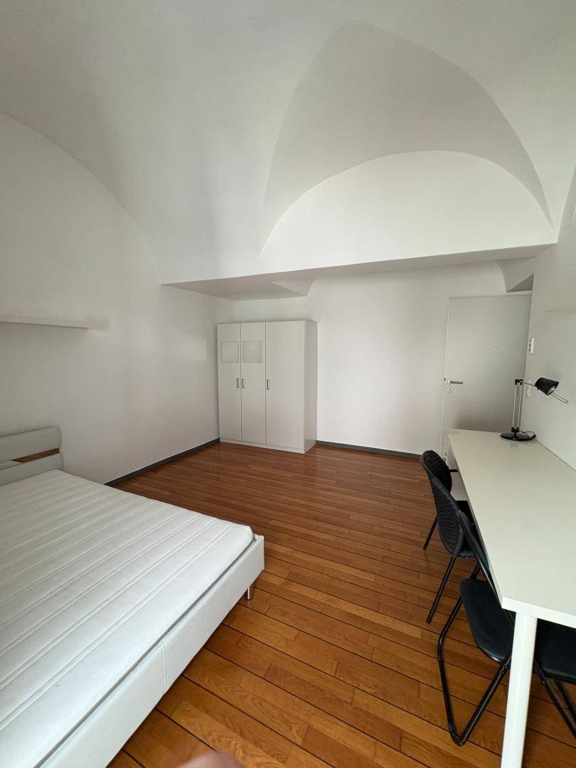 Geräumiges Schlafzimmer mit Gewölbedecke, Parkettboden und modernem Mobiliar.