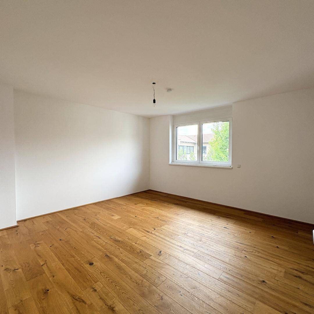 Helles Schlafzimmer mit Holzboden und großem Fenster, das viel Tageslicht hereinlässt.