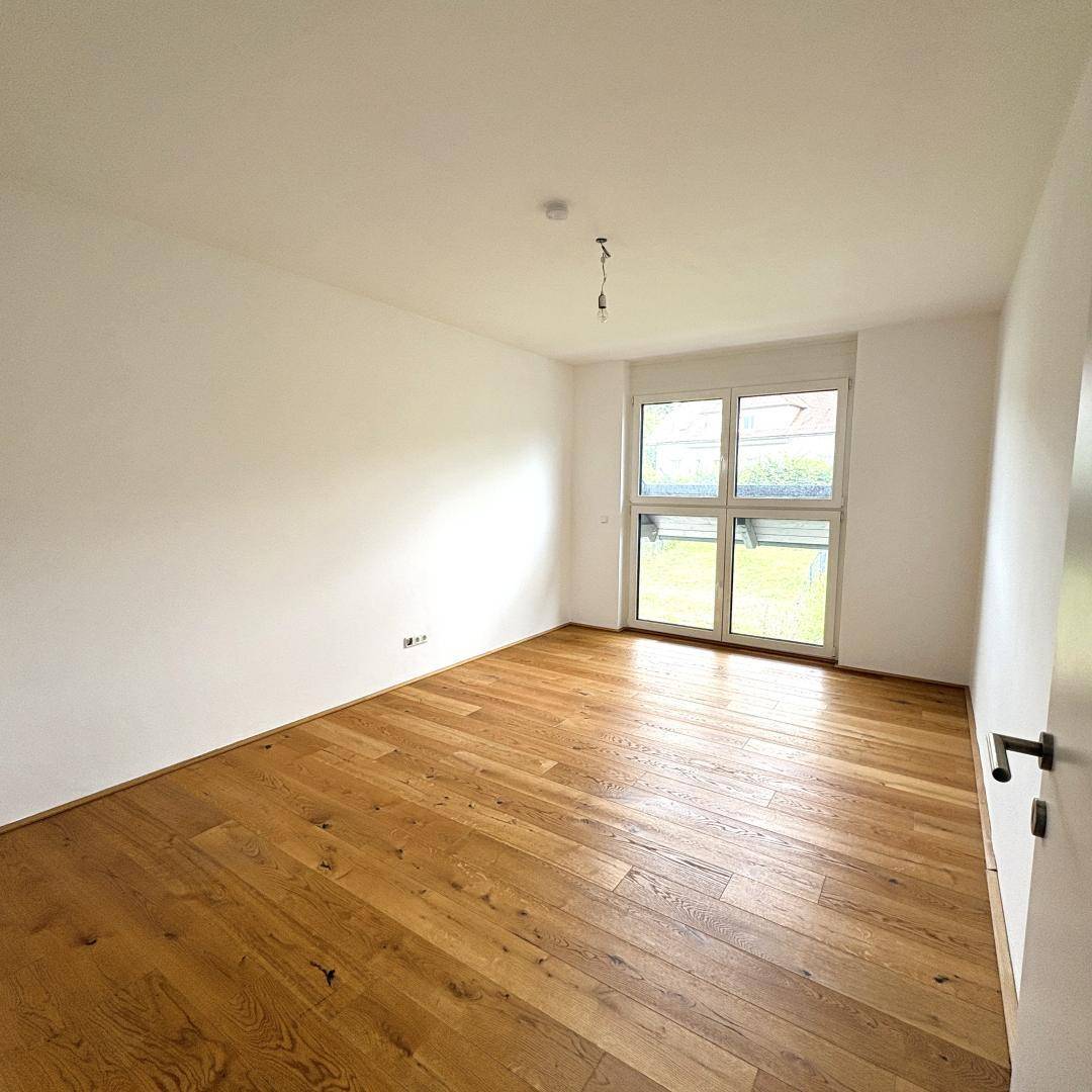 Schlafzimmer mit Holzboden und Fenster, das den Blick auf den Außenbereich freigibt.