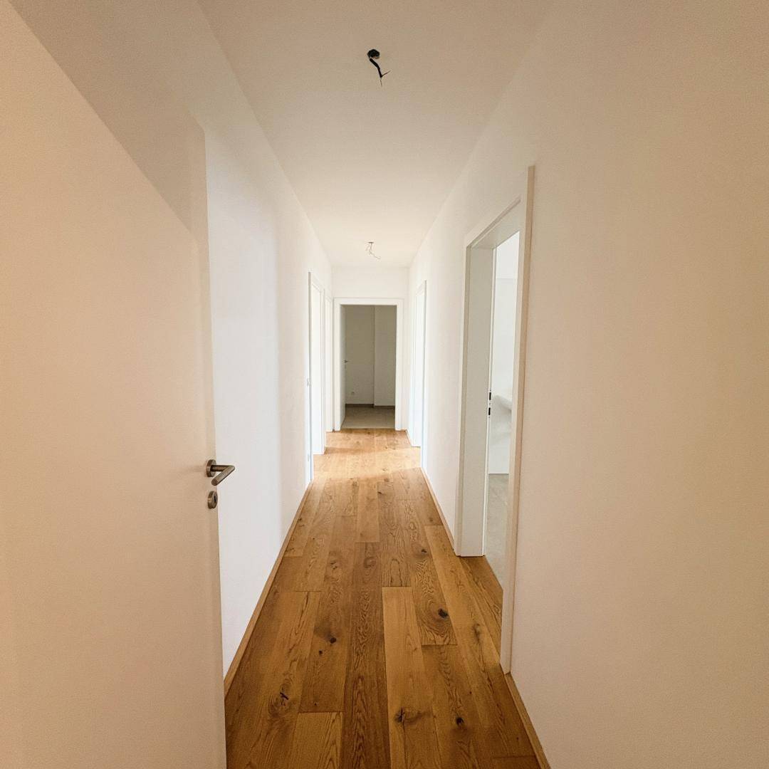 Langer, heller Flur mit Holzboden, der zu verschiedenen Zimmern der Wohnung führt.