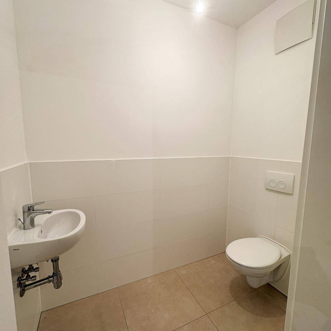 Modernes Gäste-WC mit wandhängender Toilette, kleinem Waschbecken und hellen Fliesen.