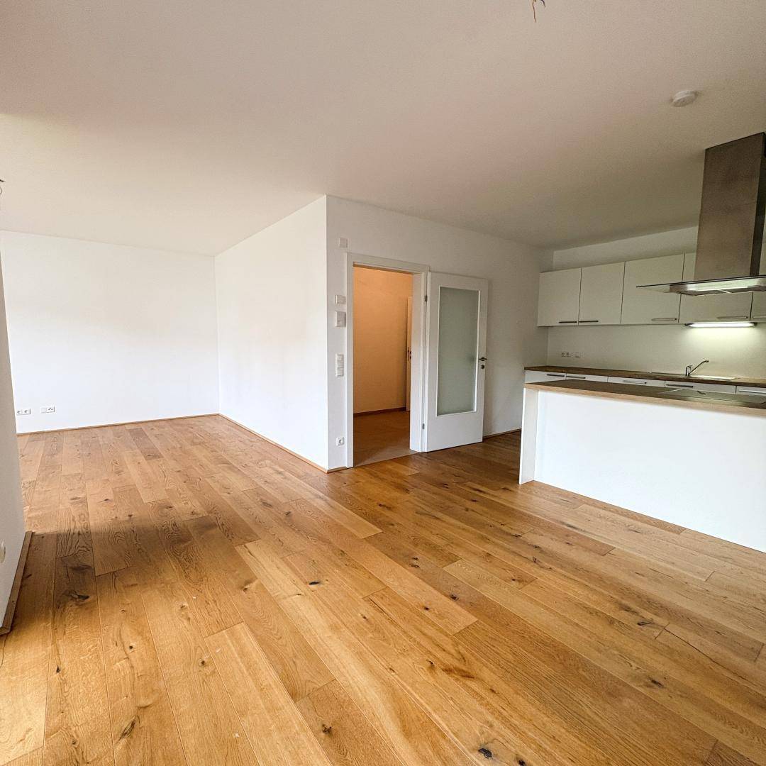Offener Wohnbereich mit Holzboden, weiß gestrichenen Wänden und Blick auf die moderne Küche.