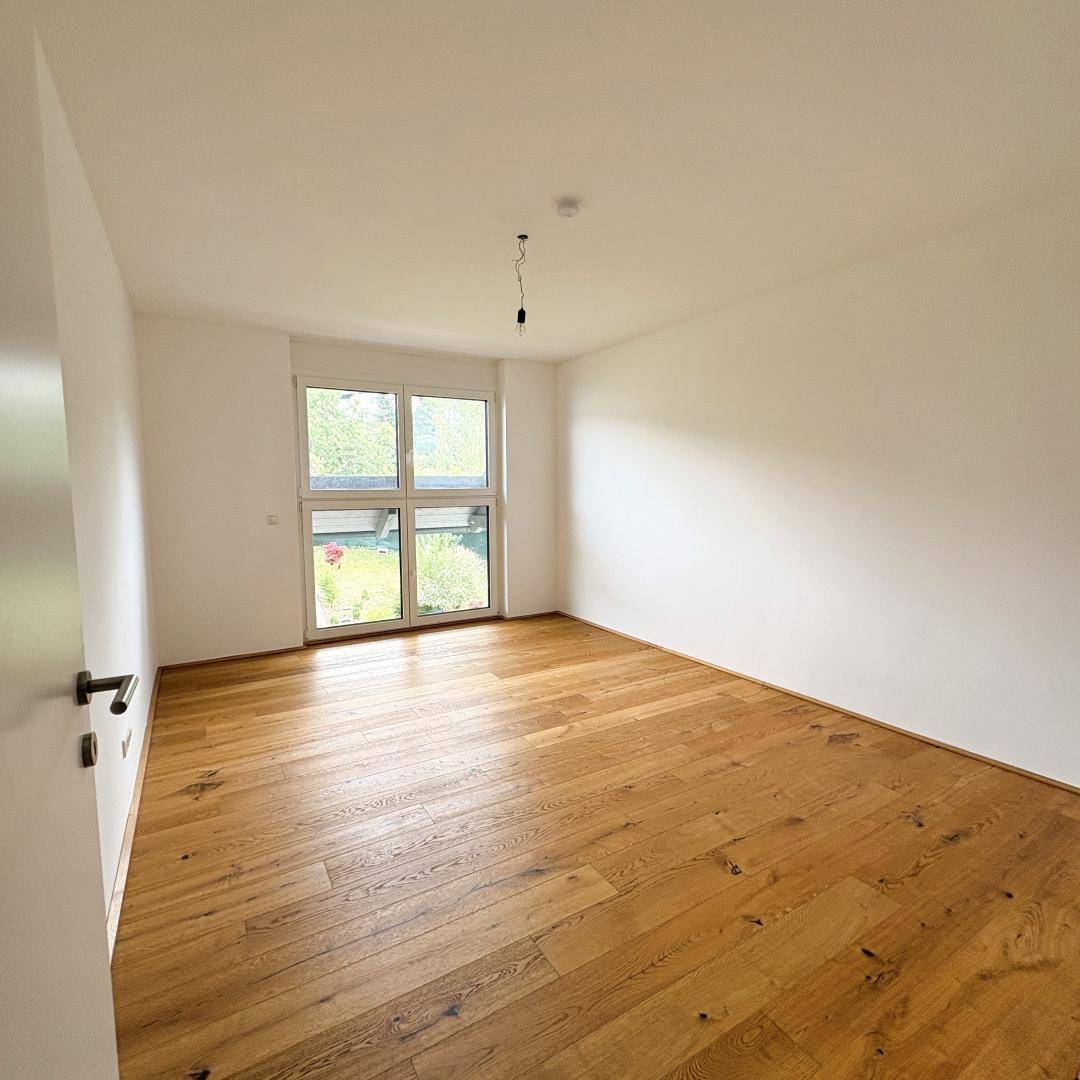 Helles Schlafzimmer mit Holzboden und Fenster mit Blick auf den Gartenbereich.