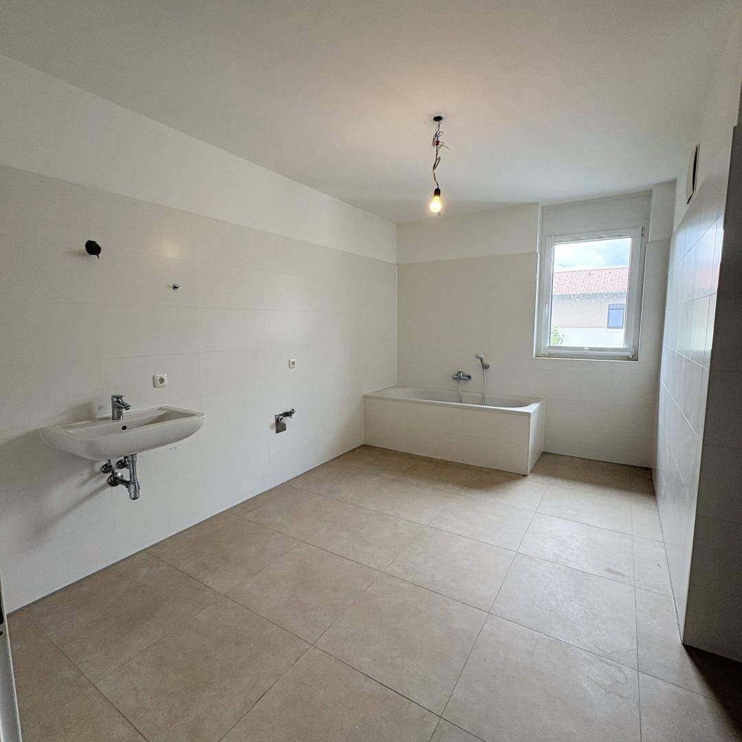 Geräumiges Badezimmer mit Badewanne, Waschbecken und hellen Fliesen, bereit für die Endmontage.