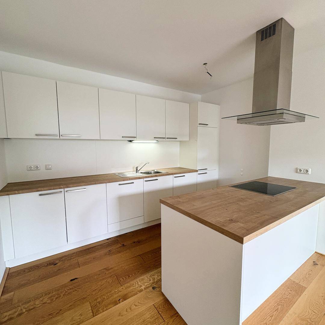 Moderne Einbauküche mit weißen Schränken, Holz-Arbeitsplatten und Kochinsel mit Induktionskochfeld.