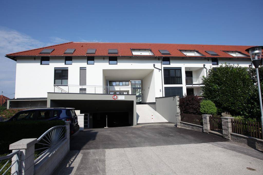 Vorderansicht einer modernen Wohnanlage mit Tiefgaragenzufahrt und rotem Ziegeldach.