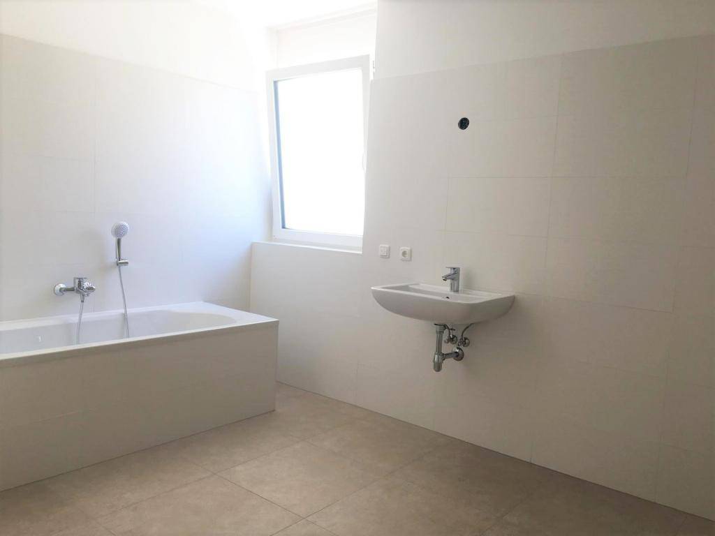Helles Badezimmer mit Badewanne, Waschbecken und einem Fenster für natürliche Belüftung.