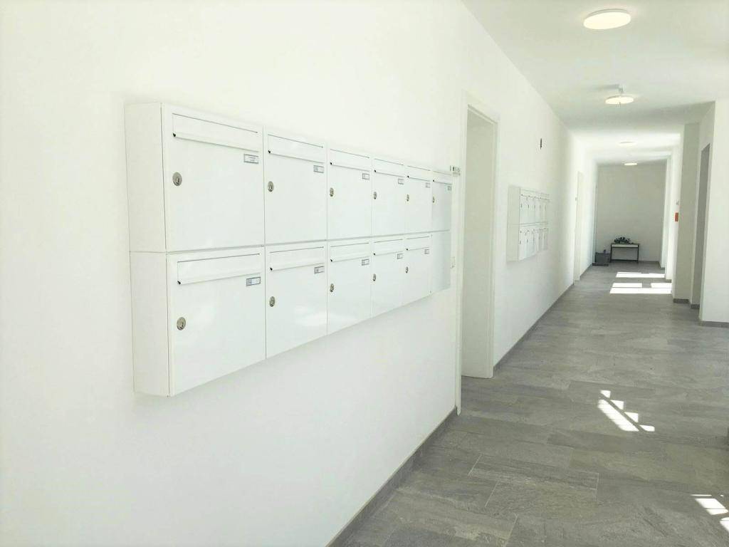 Langer, heller Flur mit Briefkästen an der Wand und Fliesenboden.