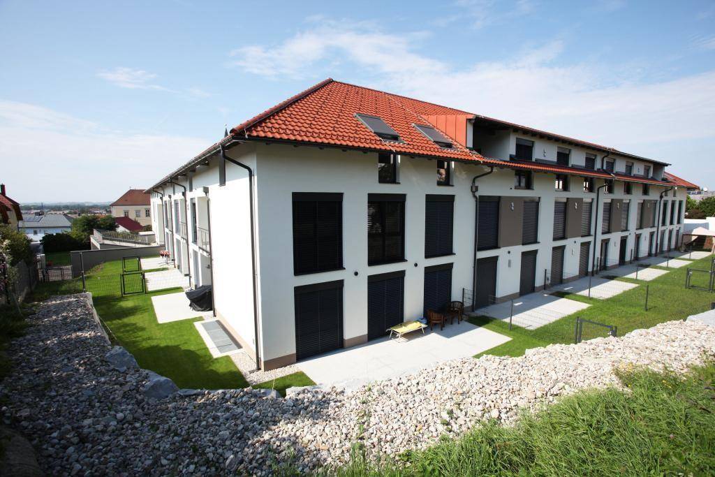 Rückansicht einer modernen Wohnanlage mit Terrassen, Rasenflächen und Rollläden an den Fenstern.