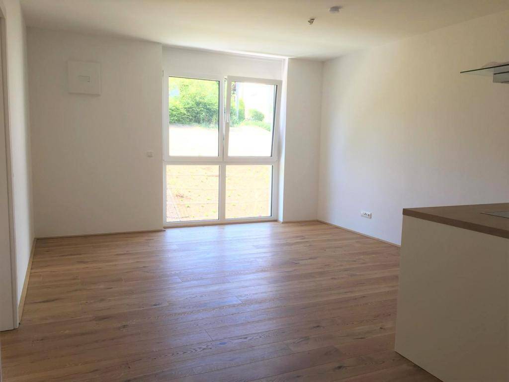 Heller Wohnbereich mit großen Fenstern und Zugang zu einem potenziellen Gartenbereich, ausgestattet mit Holzboden.