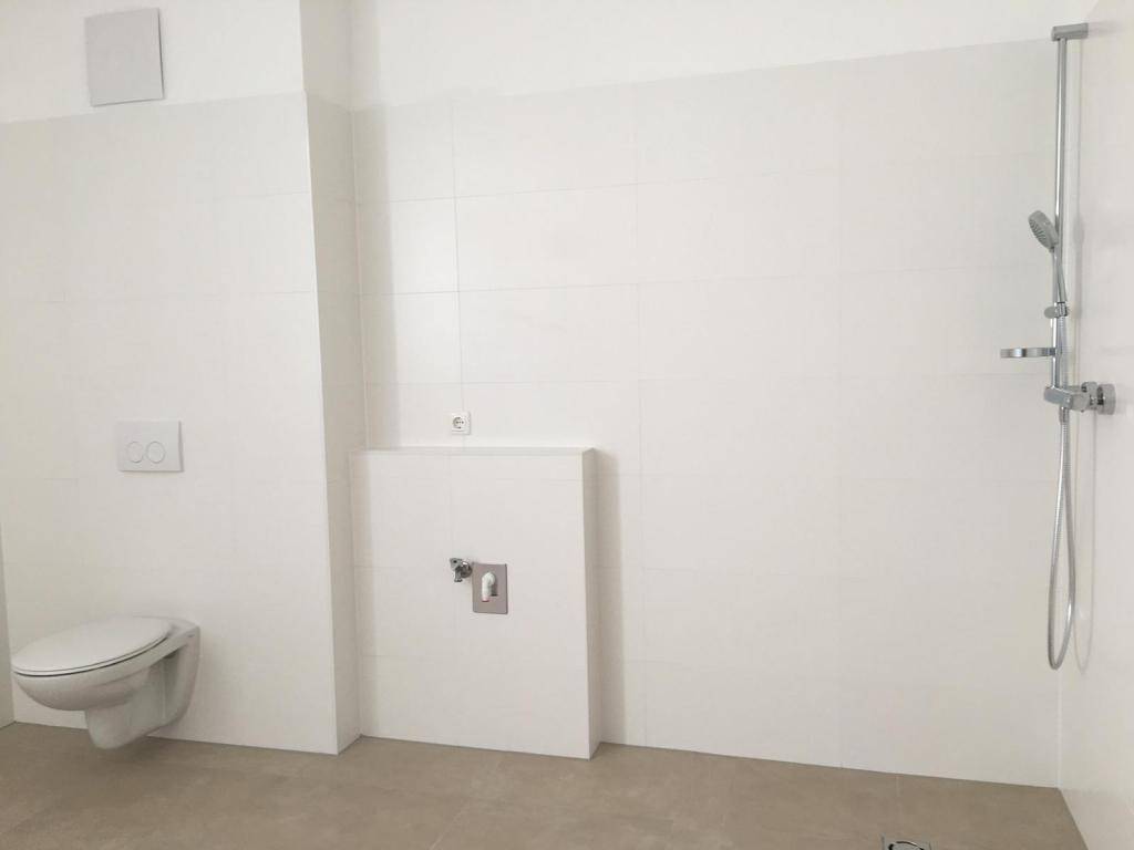 Modernes Badezimmer mit wandhängendem WC und einer geräumigen, ebenerdigen Dusche.