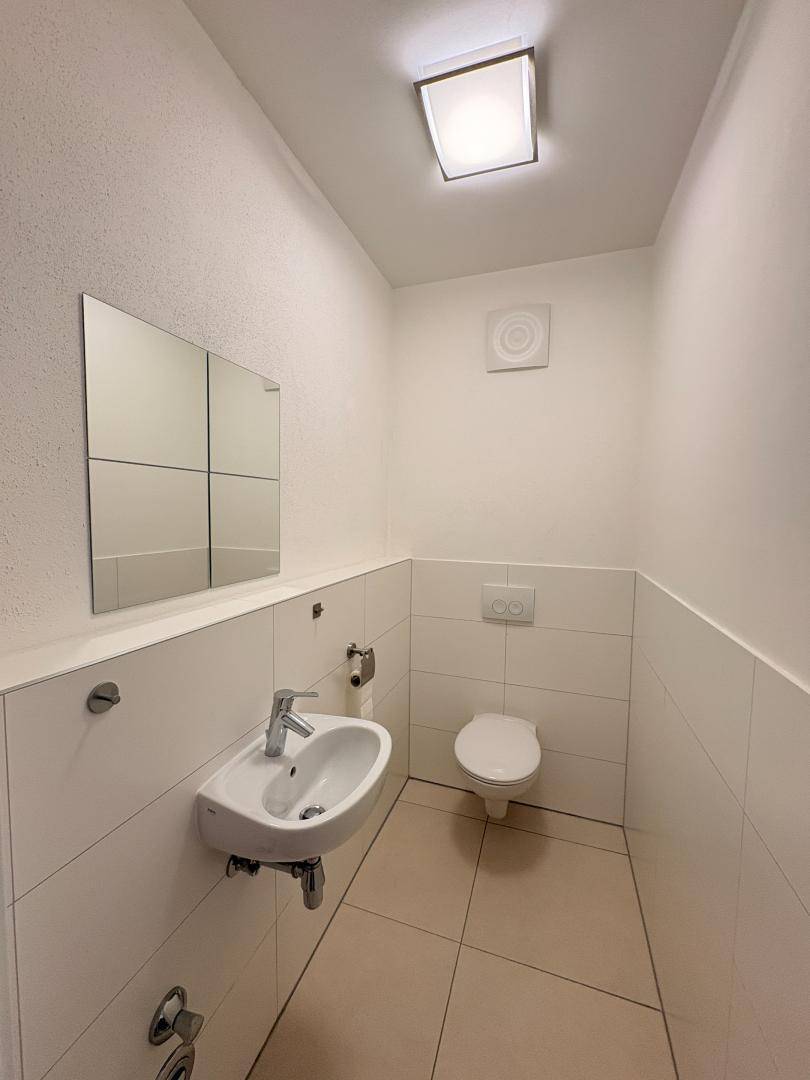 Gäste-WC mit wandhängender Toilette, kleinem Waschbecken und einem Spiegel.