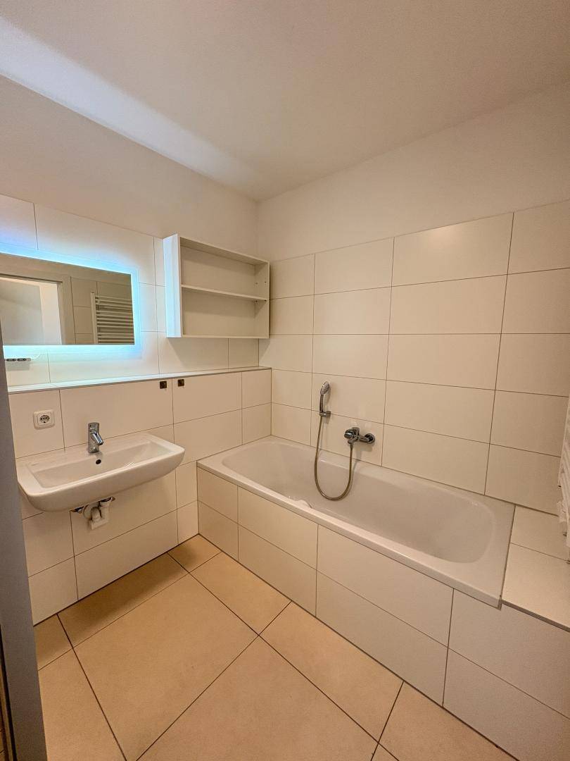 Helles Badezimmer mit Badewanne, Waschbecken und einem beleuchteten Spiegelschrank.