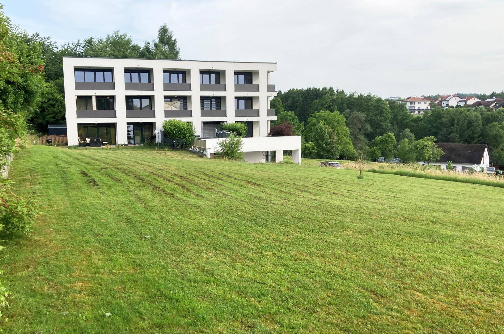 Modernes Mehrfamilienhaus mit Balkonen, eingebettet in eine grüne Hügellandschaft.