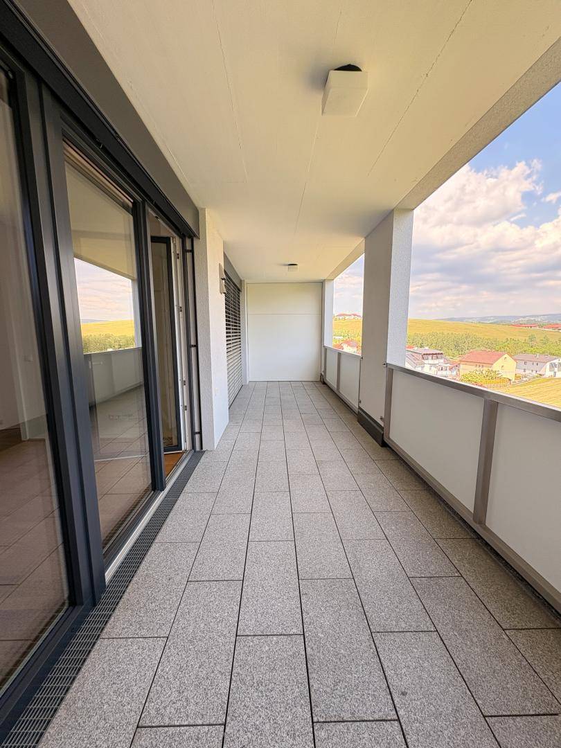 Langer Balkon mit Fliesenboden und weitem Blick über die Landschaft und Häuser.